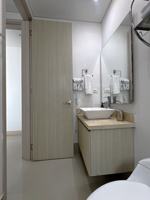 Ein modernes Badezimmer mit Holztür, Waschbecken in Weiß, einem Spiegel und einem Fön.