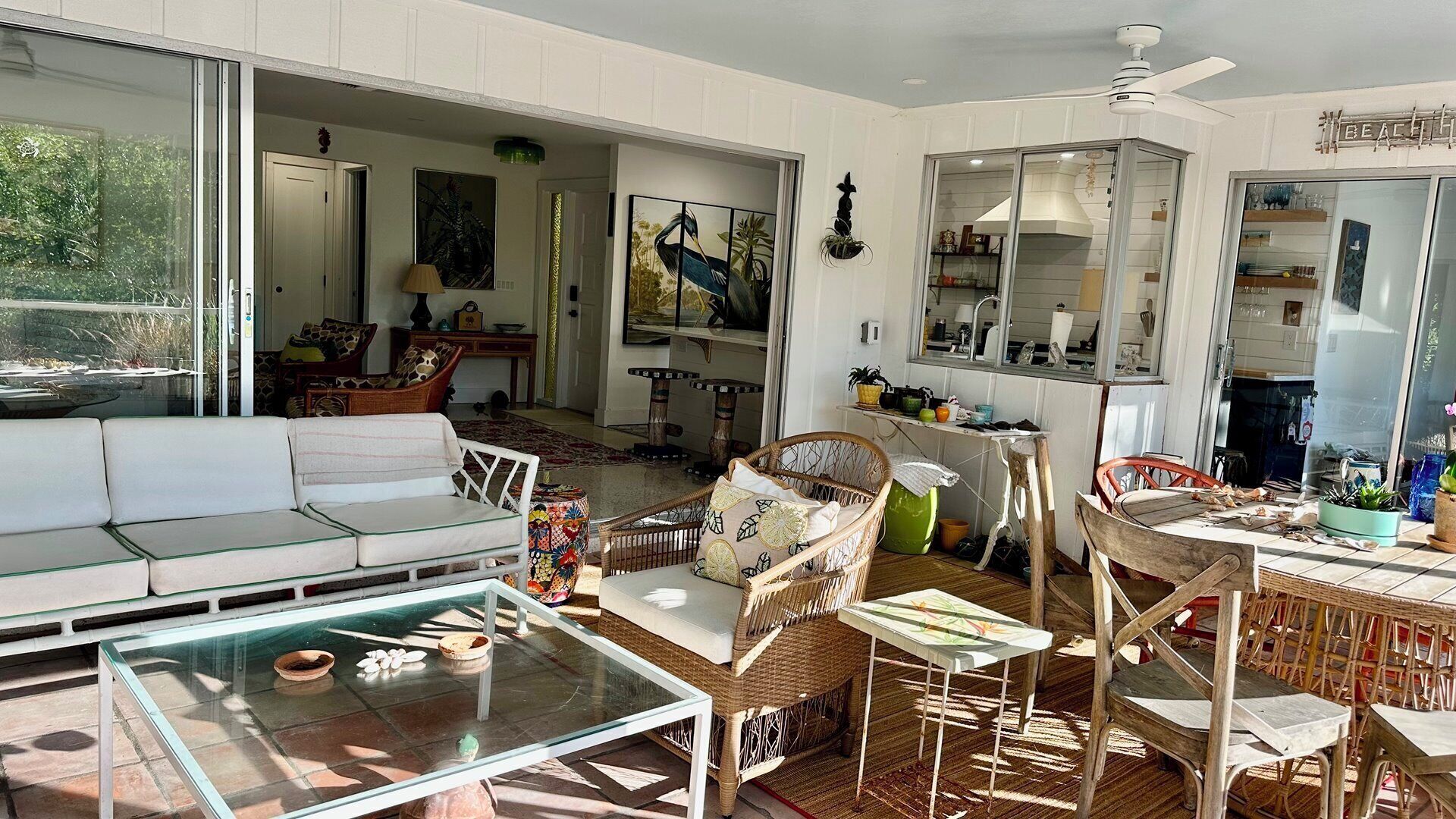 A sunlit room with a glass table, wicker furniture, and a view of the outdoors.
