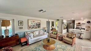 Ein Wohnzimmer mit einer Couch, Sesseln, einem Couchtisch und einer Küchenzeile mit Kühlschrank und Schränken.