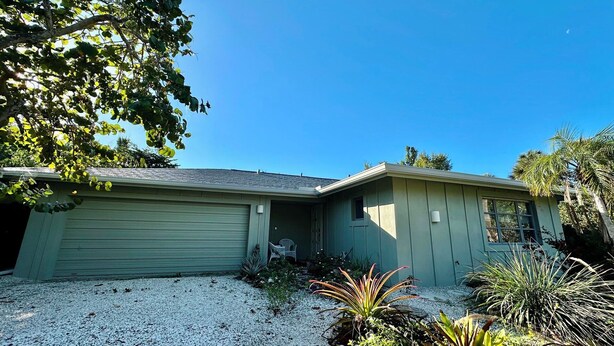 A single-story house with a garage, a covered porch, and a gravel driveway. - Shovel Sand, Not Snow! You've found your Sanibel Island retreat! Secluded near-beach Strangler Fig home has it all.  Pet-friendly, too! (Sanibel)