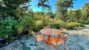 A round outdoor table with six chairs, surrounded by lush greenery and a gravel path. - Shovel Sand, Not Snow! You've found your Sanibel Island retreat! Secluded near-beach Strangler Fig home has it all.  Pet-friendly, too! (Sanibel)