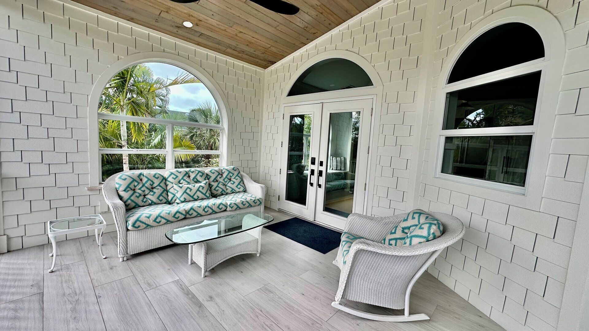 A sunlit room with a white brick wall, a sofa, a chair, and a glass door leading outside.