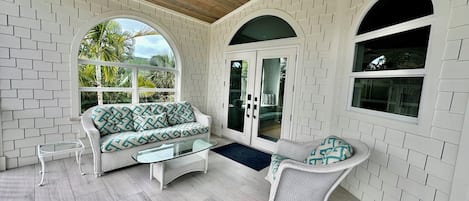 A sunlit room with a white brick wall, a sofa, a chair, and a glass door leading outside.