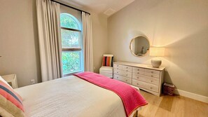 A bedroom with a bed, a dresser, a mirror, and a window with curtains. - Surf Sound - Luxury 4BR Sanibel Home, Heated Pool, Cabana 5-Min Walk to Beach (Sanibel)