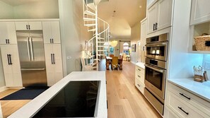 A modern kitchen with stainless steel appliances, a central island, and a spiral staircase leading to an upper level. - Surf Sound-Luxury 4BR Home, Heated Pool, Cabana, PET Friendly, Near Beach (Sanibel)