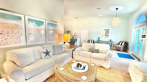 A living room with a sofa, armchairs, a coffee table, and wall art. - Surf Sound - Luxury 4BR Sanibel Home, Heated Pool, Cabana 5-Min Walk to Beach (Sanibel)