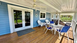 Une véranda couverte avec une terrasse en bois, des chaises en osier blanches, une table et des ventilateurs de plafond.