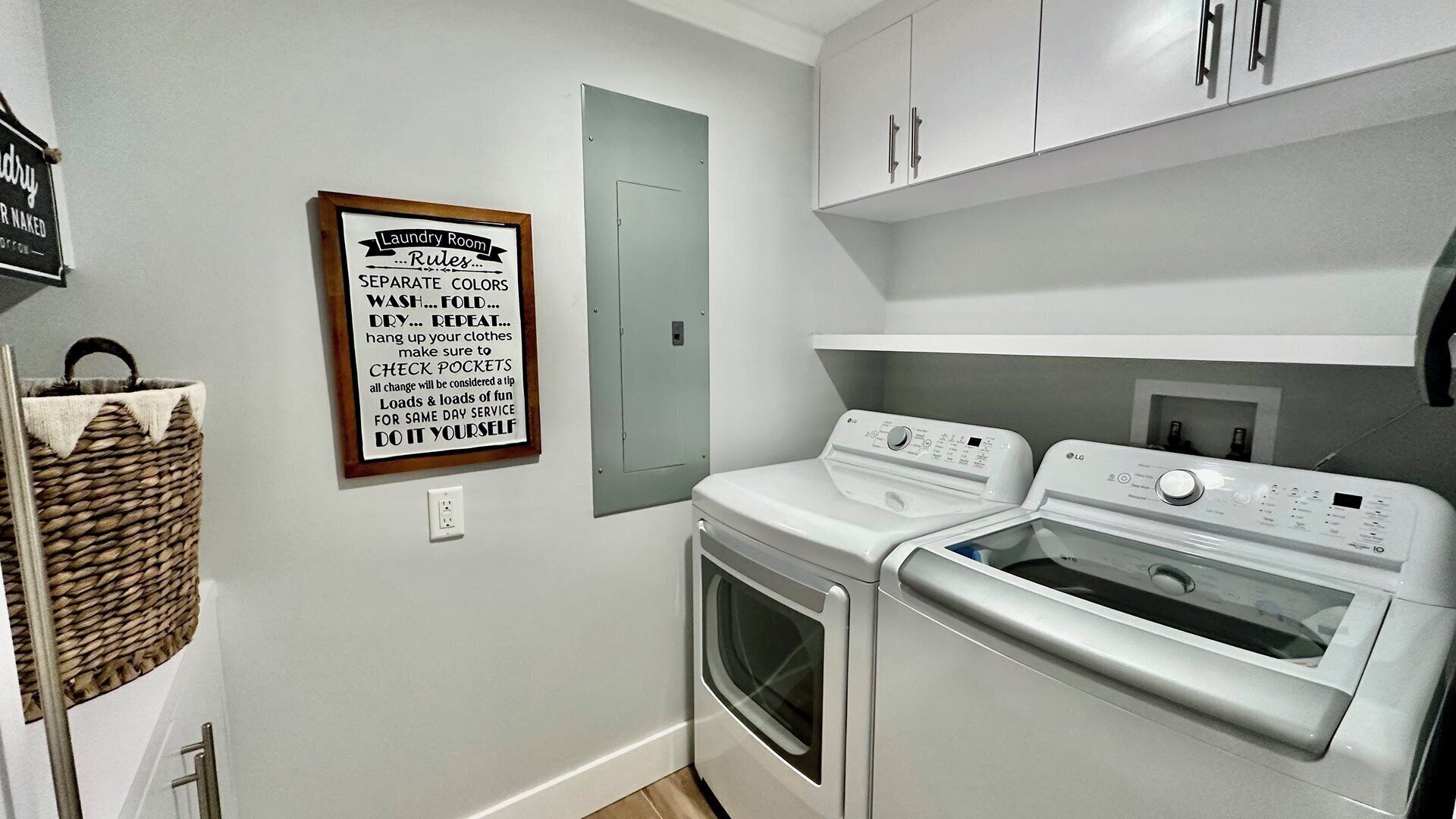 Une buanderie avec un panneau indiquant les règles à respecter pour le lavage du linge, un panier en osier et deux machines à laver LG blanches.
