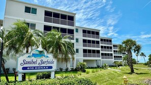 A hotel named 'Sanibel Surfside' with a modern multi-story building, a sign with a beach scene, and surrounding palm trees. - Sanibel Surfside 117 - Gulf front corner unit - All new - Sunrises & Sunsets & Gulf Views Galore! (Sanibel)