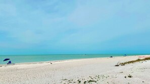 A beach with a clear sky, sandy shore, and a few people and umbrellas. - Sanibel Surfside 117 - Gulf front corner unit - All new - Sunrises & Sunsets & Gulf Views Galore! (Sanibel)