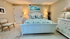 A bedroom with a bed, a chair, a dresser, a door, and a wall-mounted picture. - Sanibel Surfside 117 - Gulf front corner unit - All new - Sunrises & Sunsets & Gulf Views Galore! (Sanibel)