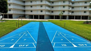 A courtyard with a shuffleboard court, a multi-story building with balconies, and a parking area. - Sanibel Surfside 117 - Gulf front corner unit - All new - Sunrises & Sunsets & Gulf Views Galore! (Sanibel)