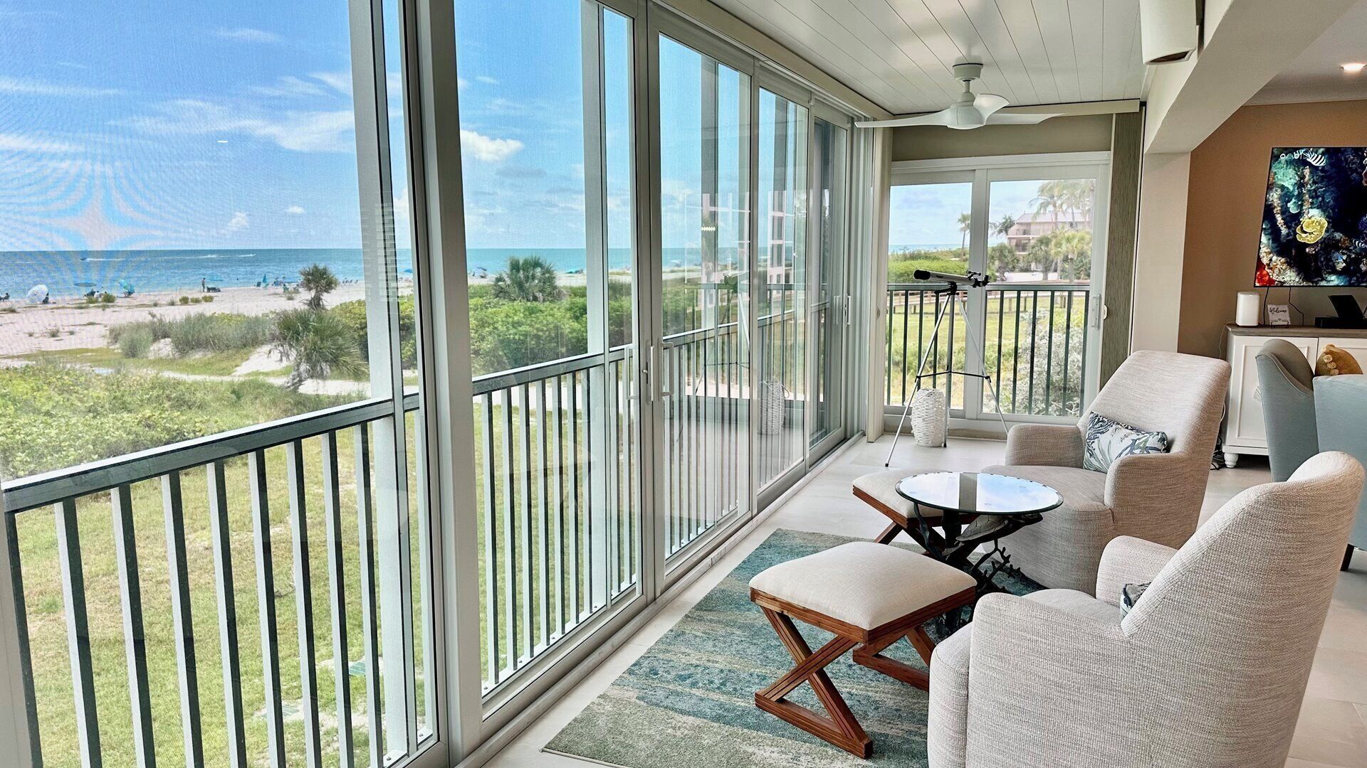 A balcony with a view of the beach and ocean, furnished with a sofa, chairs, and a small table.