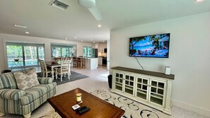 Ein geräumiges Wohnzimmer mit einem großen, an der Wand montierten Fernseher, einem Essbereich mit Tisch und Stühlen und einer gemütlichen Sitzecke mit Sofa und Couchtisch.