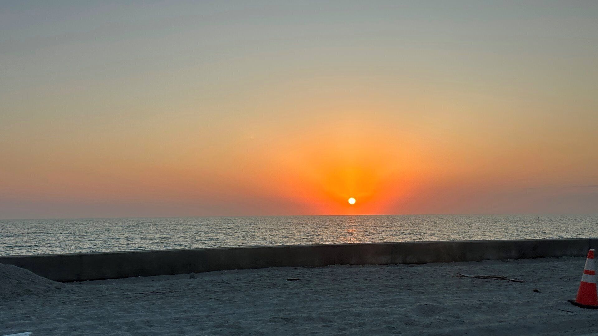 Un coucher de soleil sur l’océan, avec une barrière en béton et un cône de signalisation.