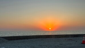Um pôr do sol sobre o oceano, com uma barreira de concreto e um cone de trânsito.