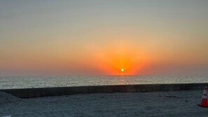 Ein Sonnenuntergang über dem Meer mit einer Betonbarriere und einem Verkehrshütchen.