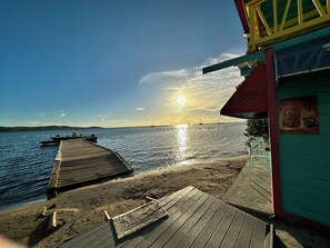 A wooden pier leading to a beach with a clear sky and the sun setting over the water.