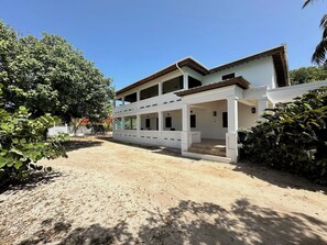 Um edifício de dois andares com varanda coberta e entrada com calçamento de areia.