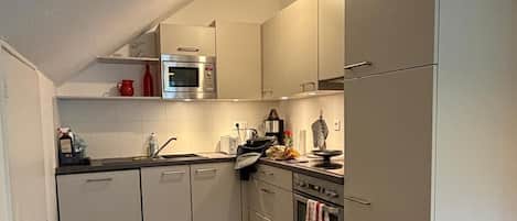 Cocina compacta con armarios blancos, microondas, estufa y lavaplatos.