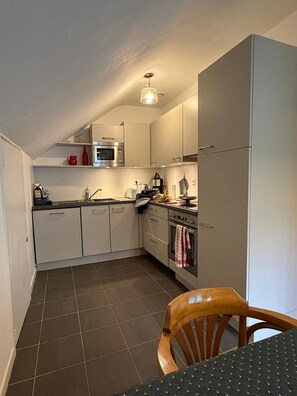 A compact kitchen with white cabinets, a microwave, a stove, and a sink. - 300m from ski slopes, 4th floor, balcony, tv, 90m², Gourette (Eaux-Bonnes)