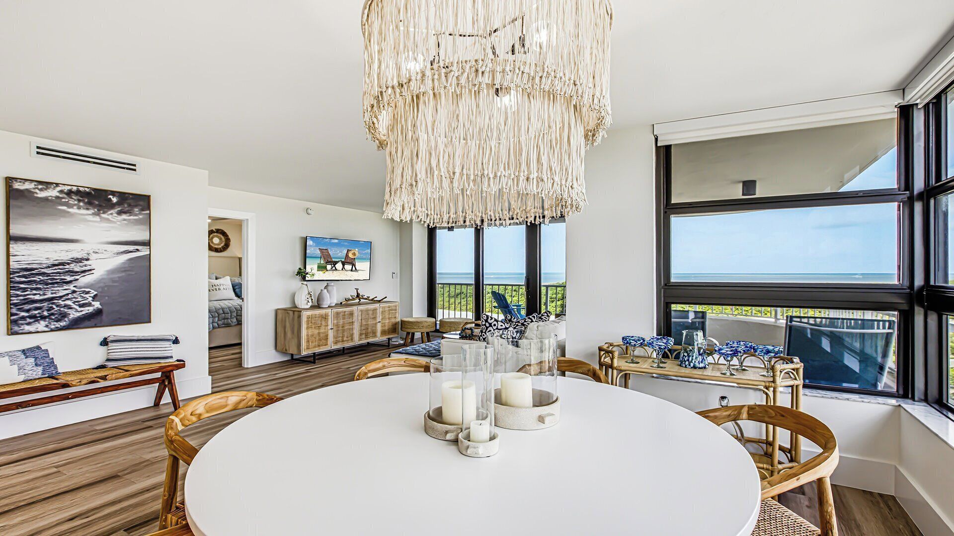 A modern dining area with a white table, candles, and wicker chairs.