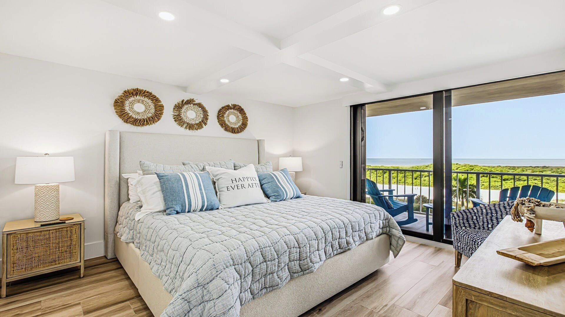 A bedroom with a large bed, two bedside lamps, a nightstand, and a view of the outdoors through a sliding glass door.