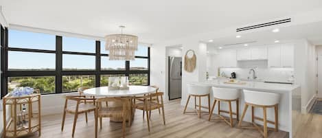 A modern kitchen with white cabinetry, a stainless steel refrigerator, and a bar area with stools.