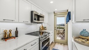 A modern kitchen with white cabinetry, a built-in oven, and a view to an outdoor balcony. - Remodeled Beachfront Corner Condo | Marco Island | Sleeps 6 (Marco Island)