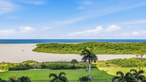A beach with a lush green area in the foreground, a clear blue sky, and the ocean in the background. - Remodeled Beachfront Corner Condo | Marco Island | Sleeps 6 (Marco Island)