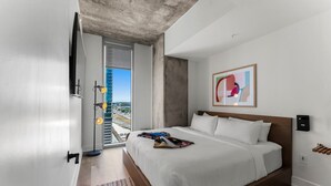 Une chambre d’hôtel moderne avec un grand lit, une vue sur le paysage urbain et un plafond en béton.