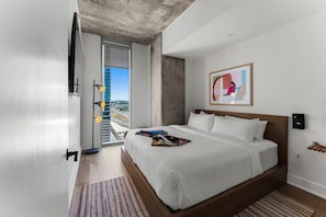 A modern hotel room with a large bed, a view of a cityscape, and a concrete ceiling. - Luxury Downtown Stay l Rooftop Pool & Skyline Views (Austin)
