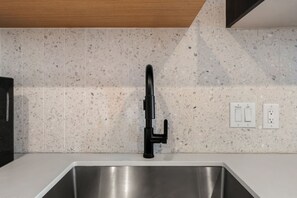 A kitchen with a stainless steel sink, a black faucet, and a backsplash with speckled tiles. - Luxury Downtown Stay l Rooftop Pool & Skyline Views (Austin)