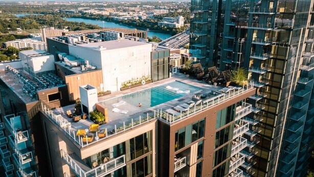Un immeuble de grande hauteur doté d’une piscine sur le toit, de nombreux balcons et offrant une vue sur une rivière et le paysage urbain.