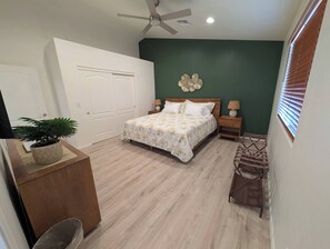 Une chambre à coucher avec un lit, des tables de chevet, un ventilateur de plafond et une fenêtre avec des stores.