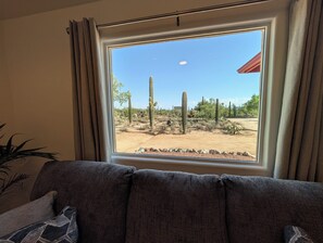 Ein Zimmer mit großem Fenster, das einen Blick auf eine Wüstenlandschaft mit Kakteen und einem klaren Himmel bietet.