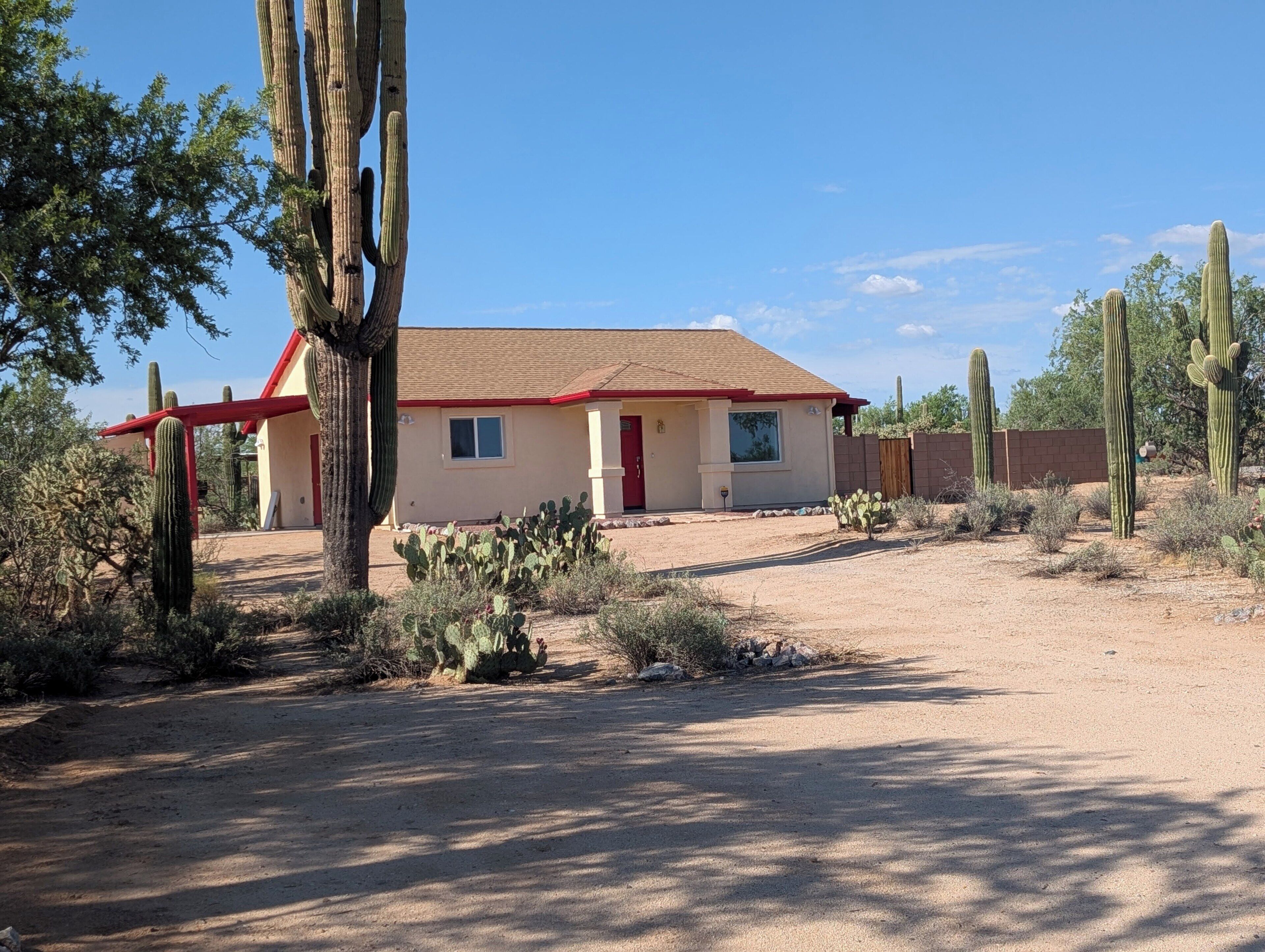 A single-story building with a red roof and beige walls, surrounded by desert vegetation and cacti.