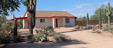 A single-story building with a red roof and beige walls, surrounded by desert vegetation and cacti.