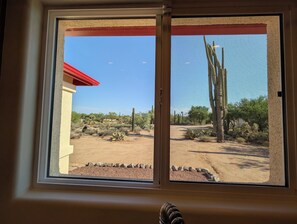 Een raam met uitzicht op een woestijnlandschap, inclusief cactussen en schaarse vegetatie.