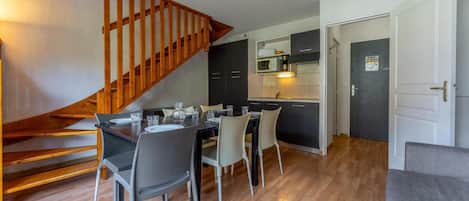A modern kitchen with dark cabinets, a wooden staircase, and a dining area with a table and chairs.