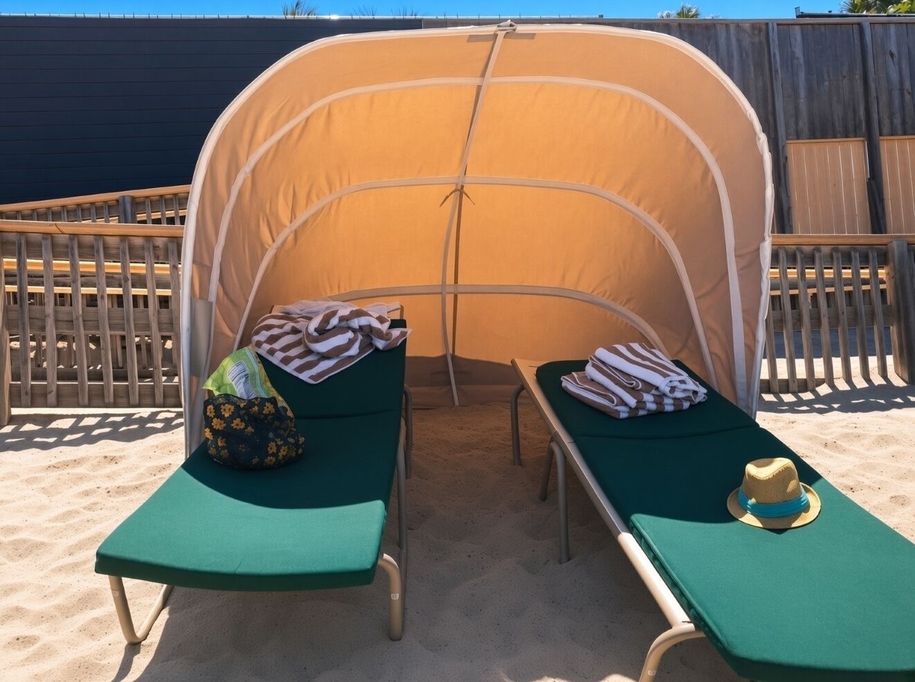 Ett tält vid stranden med två gröna solstolar, var och en med en handduk och en hatt.