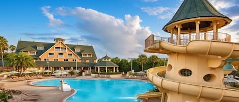 Un resort con una amplia piscina, una torre con techo cónico y un edificio con varios balcones.