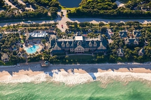 An aerial view of a resort with a large building, a swimming pool, and a beach.