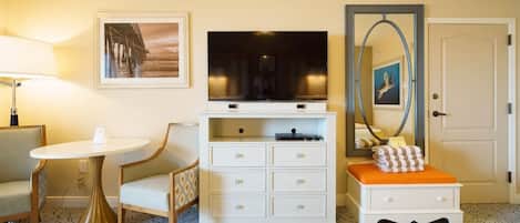 A hotel room with a television, a desk, a chair, a bedside table, and a bed.