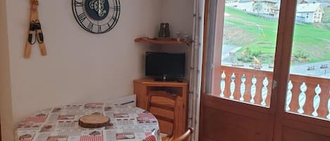 Ruokailutila, jossa on kahdelle katettu pöytä, seinäkello ja televisiotelineessä oleva televisio.