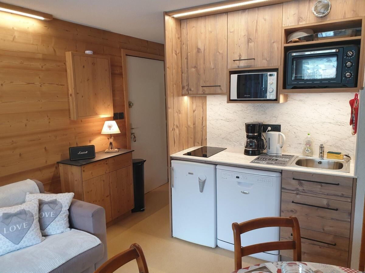 A compact kitchen with wooden cabinets, a microwave, a coffee maker, and a small refrigerator.