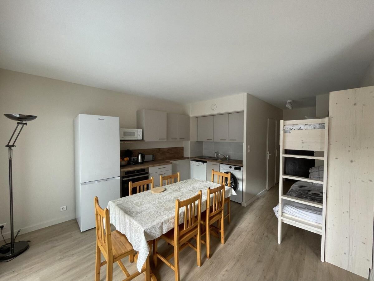 A compact kitchen with a dining table, chairs, a refrigerator, and a washing machine.