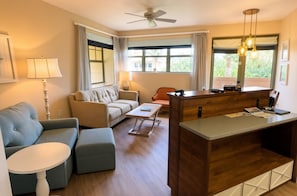 A modern living room with a sofa, a coffee table, a desk with a computer, and a ceiling fan.
