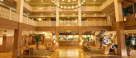 A multi-level hotel lobby with a grand chandelier, wooden railings, and a central reception desk.