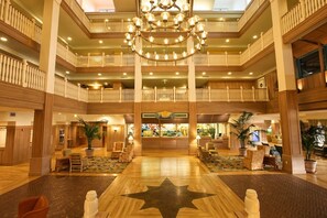 A multi-level hotel lobby with a grand chandelier, wooden railings, and a central reception desk.